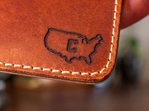 A close-up of the KC Laser Co Slim Leather Wallet, handcrafted with brown leather and white stitching, shows an embossed USA outline highlighting Colorado. Made in the USA with 6 pockets.