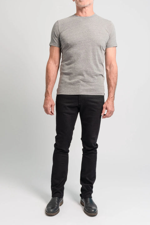 A man, partially out of the frame, stands against a plain background wearing a grey t-shirt, black shoes, and The Nelson Black Denim slim cut jeans by Marc Nelson.