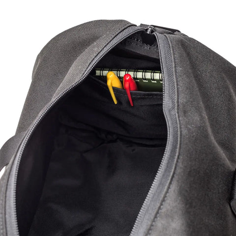 The MIS Training Drum Bag Small - Black, made from 1000D Dupont Cordura Nylon with a heavy-duty YKK zipper, is unzipped to show a green spiral notebook and two pens—yellow and red—clipped on top; nothing else is inside.