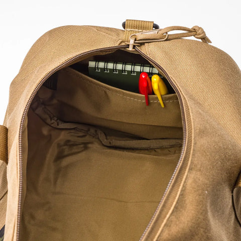 The MIS Training Drum Bag Small in Coyote Brown is shown open, revealing a spiral notebook and two pens—one red, one yellow—in an inner pocket against a plain white background.