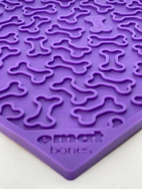 A close-up of the SodaPup Bones Design EMat Enrichment Lick Mat in purple silicone with a raised bone pattern. e mat bones is embossed in the corner, making it ideal for promoting dog licking benefits.