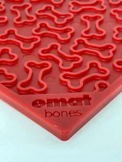 Close-up of the SodaPup Bones Design EMat Enrichment Lick Mat in red silicone, featuring raised bone patterns and emat bones embossed on the corner—ideal as a dog enrichment toy.