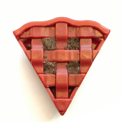 The SodaPup Cherry Pie EChew Ultra Durable Nylon Dog Chew Toy and Treat Holder features a red lattice crust with a soil-like filling, resembling a quirky pie slice for power chewers, set on a plain white background.