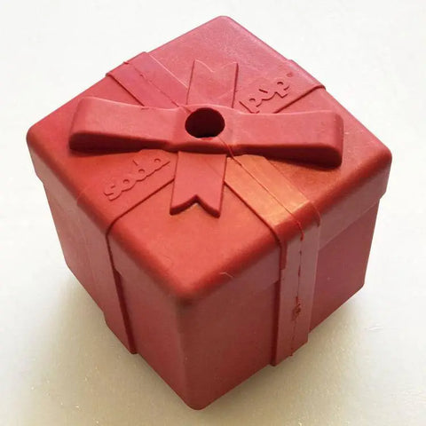 The SodaPup Gift Box EDispenser is a red, cube-shaped durable rubber chew toy and treat dispenser designed to look like a gift box with a bow and a hole in the lid.