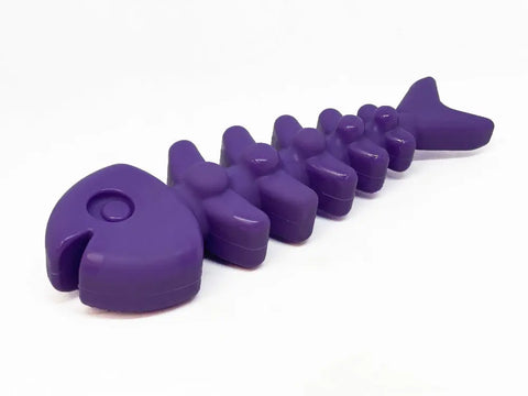 The SodaPup Fish Bone Ultra Durable Nylon Chew Toy is a purple, fish skeleton-shaped toy with a large head, segmented spine, and tail—ideal for power chewers and reducing problem behaviors—all shown on a white background.