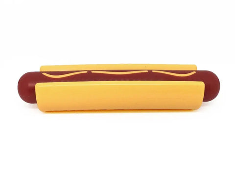 The SodaPup Hot Dog Ultra Durable Nylon Dog Chew Toy, shaped like a hot dog with a brown sausage, yellow bun, and mustard detail, is designed to help reduce problem behaviors. Shown on a plain white background.