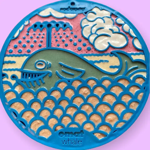 A round, colorful Whale Design EMat Enrichment Lick Mat With Suction Cups by SodaPup features a stylized whale spraying water, ocean waves, pink and beige background, blue border, and the words omai whale at the bottom.