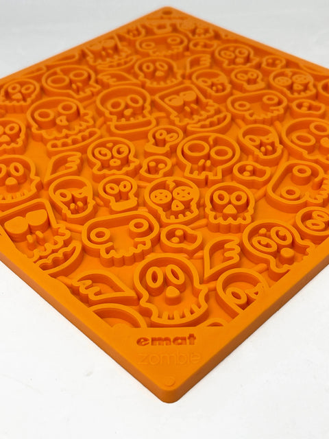 The SodaPup Zombie Design Emat Enrichment Lick Mat is an orange silicone treat and enrichment mat for dogs, featuring raised cartoon skull and bone shapes, with emat zombie embossed in one corner for added fun.