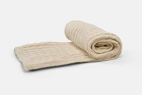 The American Blossom Linens Cotton Knitted Baby Blanket, shown partially unrolled on a light background, features a beige color and textured wavy pattern—ideal for use in a crib or stroller.