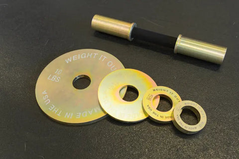 Four gold-colored calibrated plates and a small metal bar with black grip from the Weight It Out Solid Steel Loadable Dumbbell Sets are displayed. The largest plate is labeled 10 lbs, Weight It Out, Made in the USA.