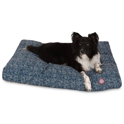 A black and white dog is lying on a Majestic Pet South West Rectangle Dog Bed with a removable cover and blue pattern, looking toward the camera.