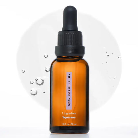 An upright brown glass dropper bottle labeled Open Formula Squalane stands with droplets scattered nearby and a soft, circular background—ideal for deeply moisturizing your skin.