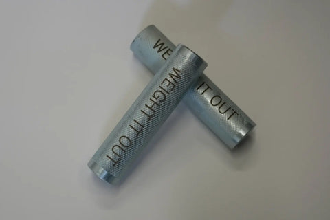 Two Dumbbell Standard 1 Handle Screwable Pair by Weight It Out intersect on a white background. Each metal handle features a textured grip, with one engraved WEIGH IT OUT and the other partially showing WE.