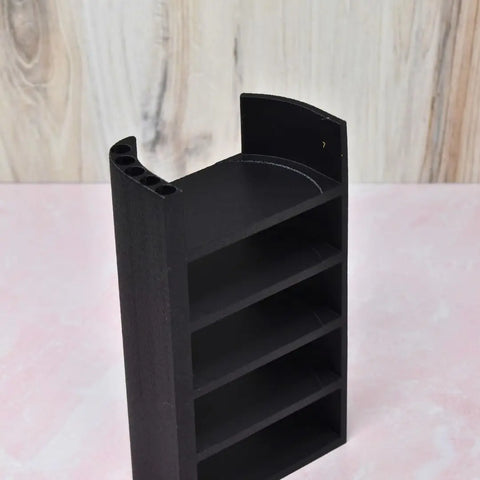 The Chatelet Manufacturing Lid Organizer Compatible With Stanley Cup Lids features four shelves, storage for five lids and straws, a curved top, and is perfect for kitchens or cabinets. Shown in black on a pink surface with a light wood background. Made in USA.