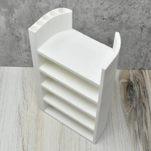 The Chatelet Manufacturing Lid Organizer—compatible with Stanley Cup lids—features four shelves, storage for straws, and five round holes on top left; perfect for cabinets or counters. Shown on a light wood surface against a gray textured wall.