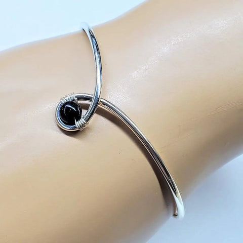 The Sterling Silver Blue Bead Ribbon Child Abuse Awareness Teardrop Bangle by Alexa Martha Designs features a minimalist looped design and is perfect for subtly showing support and awareness.
