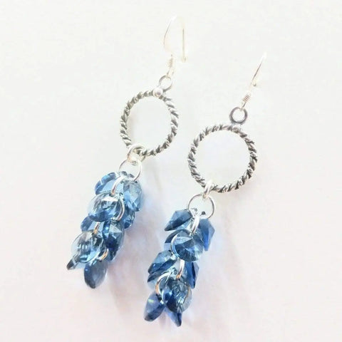 The Sterling Silver Denim Blue Crystal Cluster Earrings by Alexa Martha Designs feature textured circular hoops adorned with faceted denim blue crystal beads.