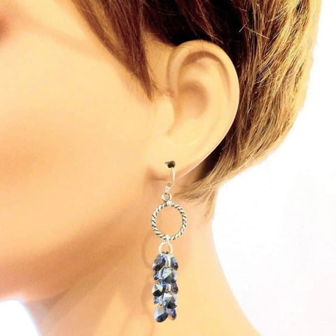 A mannequin with short brown hair showcases the Sterling Silver Denim Blue Crystal Cluster Earrings by Alexa Martha Designs, featuring a twisted design and a cluster of denim blue crystal beads.