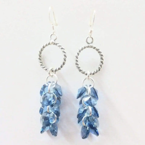 Sterling Silver Denim Blue Crystal Cluster Earrings by Alexa Martha Designs feature clusters of faceted denim blue crystals on hoops, shown against a plain white background.