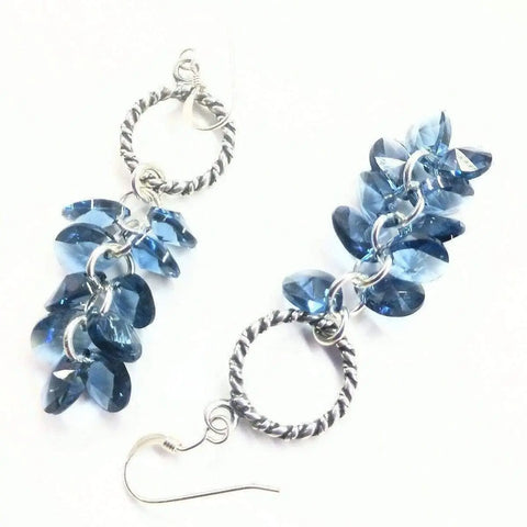 Sterling Silver Denim Blue Crystal Cluster Earrings by Alexa Martha Designs showcase twisted hoops adorned with faceted blue crystal beads, elegantly displayed on a white background.