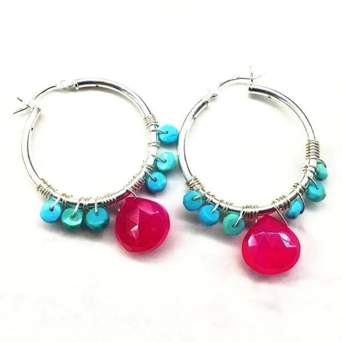The Pink and Sleeping Beauty Turquoise Silver Wire Wrap Hoop Earrings by Alexa Martha Designs feature handmade sterling silver hoops adorned with small turquoise beads and a large faceted pink bead, displayed flat on a white background.