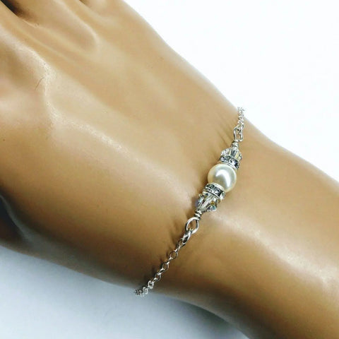 The Silver Swarovski Crystal Pearl Bar Bridal Bracelet by Alexa Martha Designs, featuring a silver chain, white pearl, and Swarovski accents, is showcased on a mannequin hand against a plain white background.