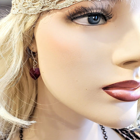 Close-up of a mannequin’s face showcasing Alexa Martha Designs’ Sterling Silver Red Heart Crystal I Love You Jesus Earrings, styled with blonde hair, deep red lips, a gold lace headband, and a chic necklace for added elegance.