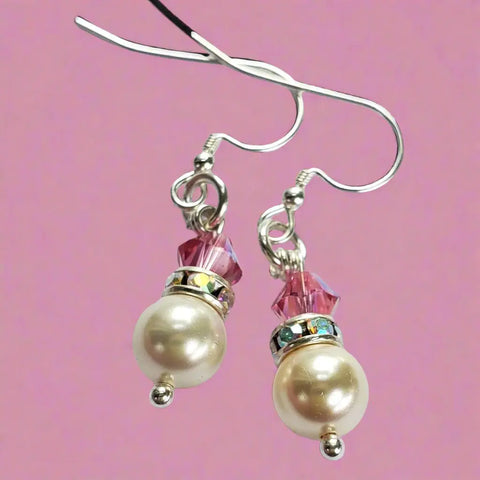 The Alexa Martha Designs Silver Swarovski Crystal Pearl Stack Earrings feature large pearl and pink crystal beads with silver hooks, shown against a pink background.