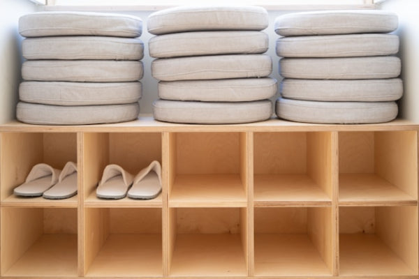 Stacks of beige cushions on a wooden shelf with a pair of sandals below.
