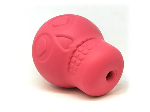 The SodaPup Sugar Skull EDispenser is a pink rubber dog chew toy with heart-shaped eyes and a hole at the base, designed for durability and treat dispensing, shown on a white background.
