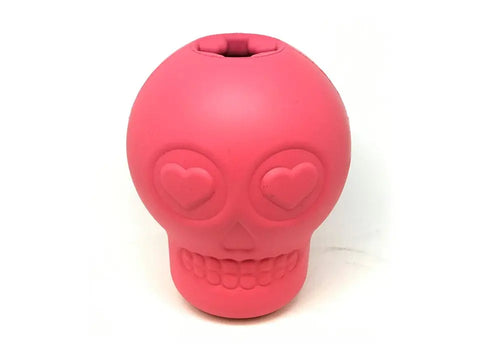 The SodaPup Sugar Skull EDispenser is a pink, durable rubber chew toy for dogs shaped like a skull with heart-shaped eyes, nose and smiling mouth details, plus a top opening for treats and a smooth, rubbery surface.