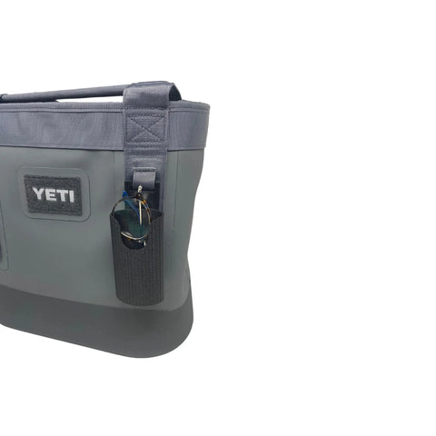 A gray YETI tote bag features a Chatelet Manufacturing Sunglasses Holder Attachment, compatible with soft Yeti coolers and backpacks, securely holding a pair of sunglasses against a plain white background.