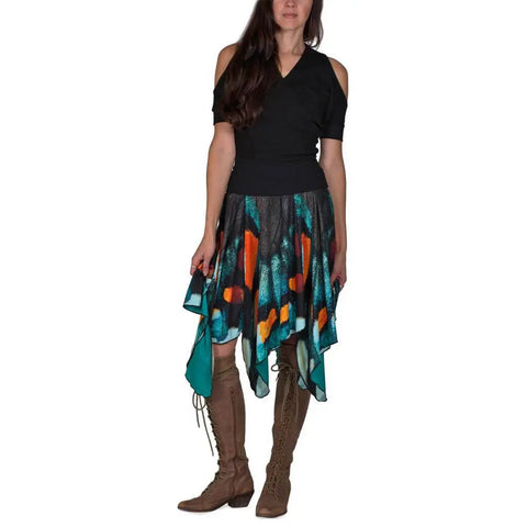A woman in a black cold-shoulder top, the Mt. Pisgah Butterfly Skirt by Spiritex | Sustainable Apparel, and knee-high lace-up brown boots stands against a white background.