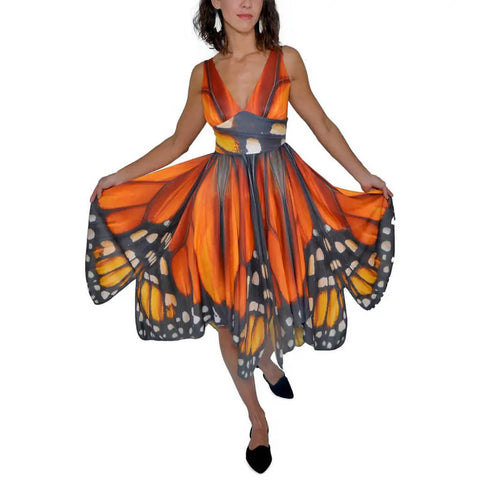 A woman wears the Monarch Butterfly Dress by Spiritex | Sustainable Apparel, featuring bold orange, black, and white wing patterns on recycled PET fabric as she spreads the striking skirt to showcase its eco-friendly design.