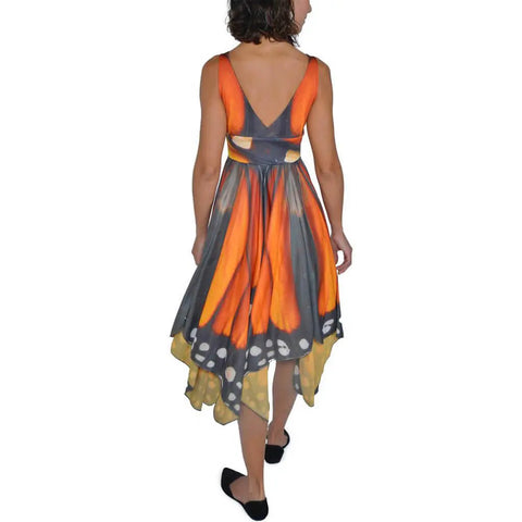 A woman with shoulder-length hair showcases the Spiritex Monarch Butterfly Dress, featuring orange, black, and white patterns inspired by butterfly wings. She completes her standout look from the sustainable brand with classic black shoes.