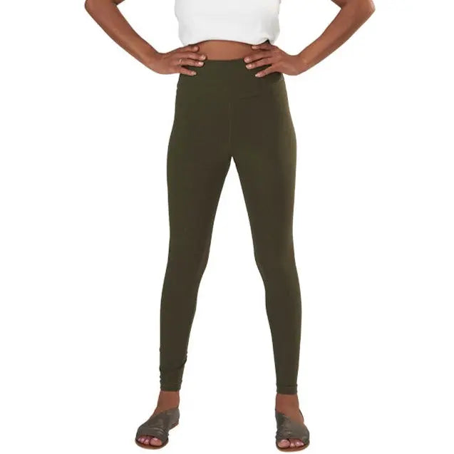 A person wearing a white crop top, Spiritex | Sustainable Apparel Yoga Leggings in high-waisted olive green (made in USA), and black slide sandals stands with hands on hips against a plain white background.