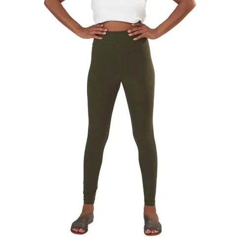 A person wearing a white crop top, Spiritex | Sustainable Apparel Yoga Leggings in high-waisted olive green (made in USA), and black slide sandals stands with hands on hips against a plain white background.