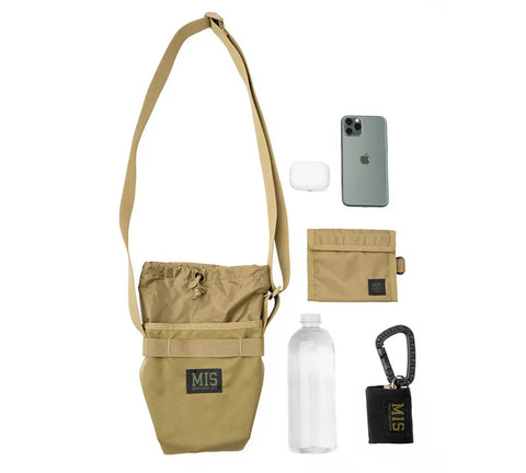 The MIS AB Shoulder Pouch in Coyote Tan, made in the USA, is shown neatly arranged next to a smartphone, white wireless earbuds case, matching tan wallet, clear water bottle, and black carabiner keychain holder with MIS label.
