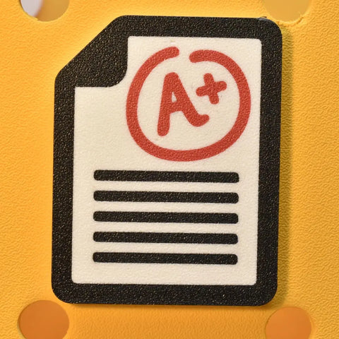 The FRESHe Baglets Teacher Charm by Chatelet Manufacturing features a cartoon paper with a circled A+—a fun decorative charm for tote bags, compatible with Bogg Bags, Simply Southern, and more; perfect for teachers.