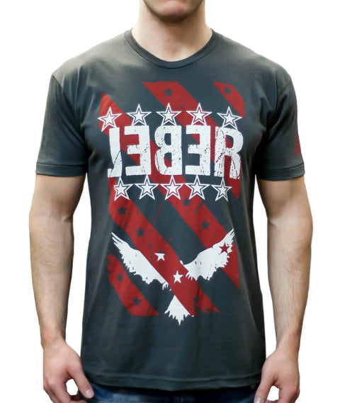 A man wearing The Defender t-shirt from Leber Apparel Line—dark gray with red stripes, white stars, two white eagles, and large distressed mirrored REBEL lettering—makes a bold patriotic statement.