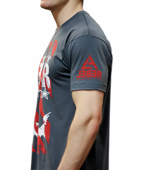 A man stands in profile against a white background, wearing The Defender dark gray graphic t-shirt from Leber Apparel Line, featuring red and white designs and a REBEL logo on the sleeve; only his upper body is visible.