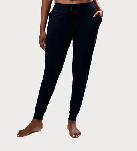 A person stands barefoot wearing Goodnighties Jogger Pants with pockets and a drawstring waist, shown from mid-torso to feet against a light gray background.