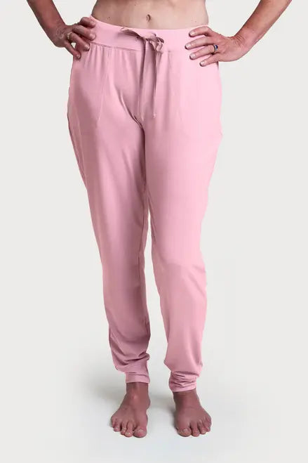A person stands barefoot, hands on hips, wearing light pink Goodnighties Jogger Pants featuring pockets and a drawstring waistband, set against a plain white background.