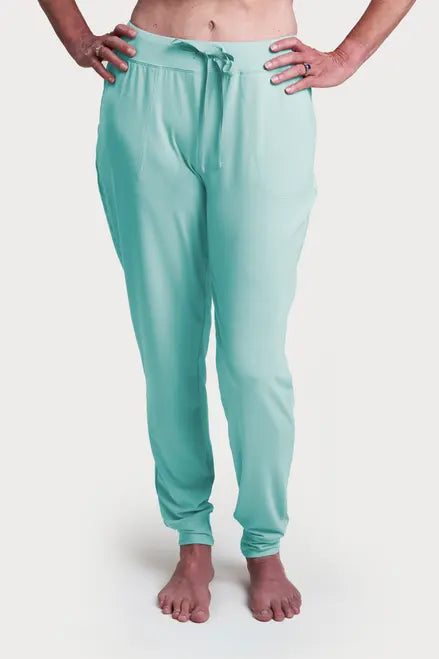 A person stands barefoot in light teal Goodnighties Jogger Pants, featuring an adjustable drawstring waist, front pockets, and innovative 37.5 technology fabric, with hands on hips against a plain white background.