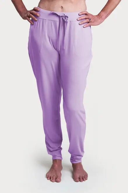 A person stands barefoot in light purple Goodnighties Jogger Pants with an elastic waistband and drawstring, hands on hips. These American-made joggers have a clean, modern look against a plain white background.