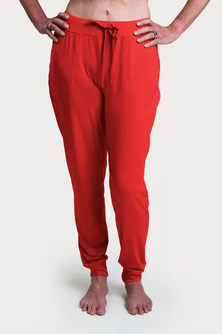 A person stands barefoot on a white background, wearing Goodnighties Jogger Pants in bright red with front pockets made from advanced 37.5 technology fabric. Only their lower torso and legs are visible, with hands resting on hips.