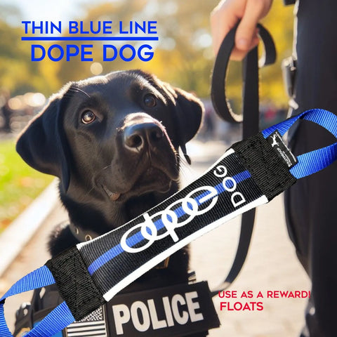 A black police dog in a POLICE vest sits by its handler with a leash. In front is the Bulletproof Pet Products Inc Thin Blue Line Dope Dog Fire Hose Training Tug, used as a K9 training reward. This durable toy also floats.