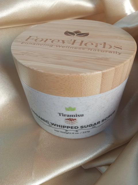 A bamboo-lidded Forev'Herbs Tiramisu Sugar Scrub jar rests on shiny beige satin. This organic 8 oz. (237g) sugar scrub highlights natural wellness and indulgence.