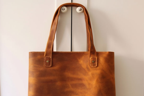 Brown leather tote bag hanging on a white door