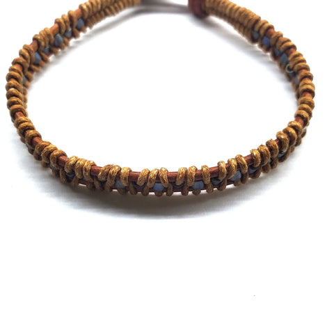 The Tree of Life Button Brown Gray Leather Wrap Seed Bead Bracelet by Alexa Martha Designs features brown cord woven with blue seed beads and a leather strand, beautifully displayed on a white background.